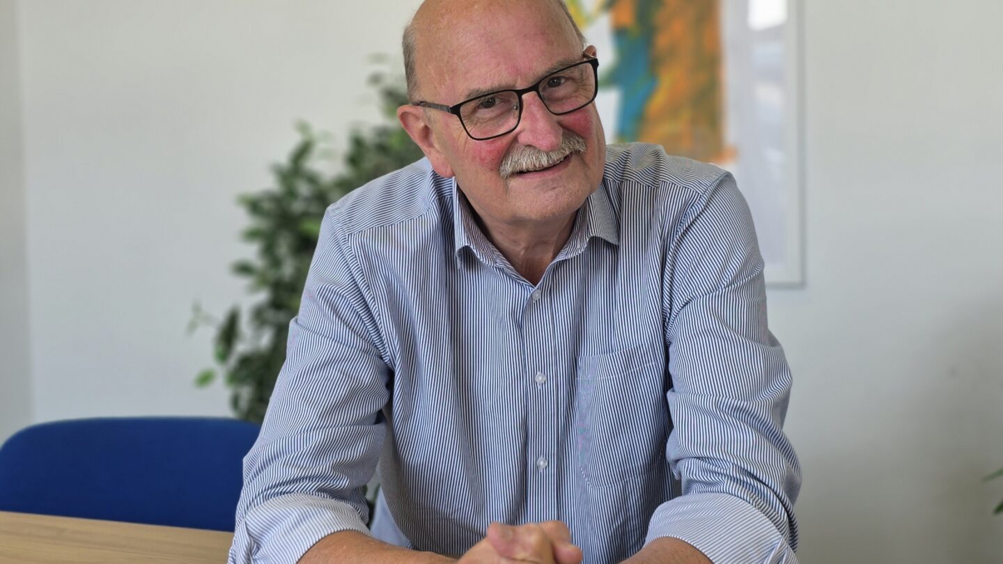 Andy Street, FareShare South West Chair of Trustees and founder. Andy is a whote man with a moustache, wearing a blue collared shirt and sitting at a desk.