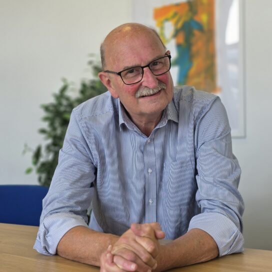 Andy Street, FareShare South West Chair of Trustees and founder. Andy is a whote man with a moustache, wearing a blue collared shirt and sitting at a desk.