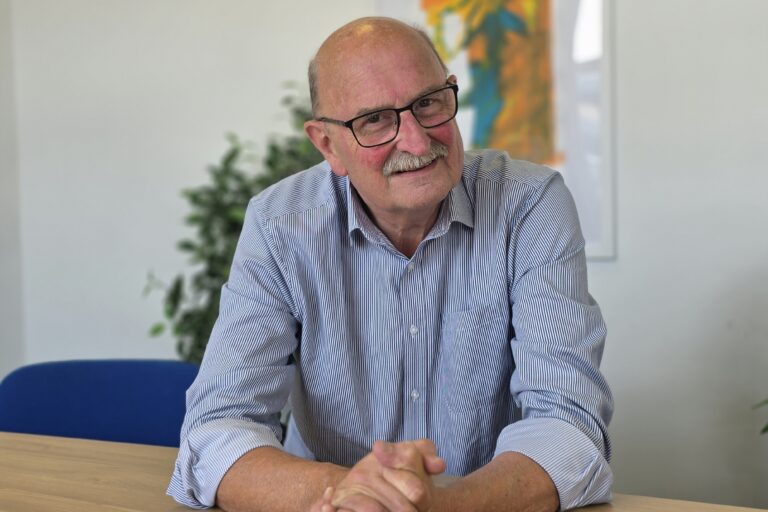 Andy Street, FareShare South West Chair of Trustees and founder. Andy is a whote man with a moustache, wearing a blue collared shirt and sitting at a desk.