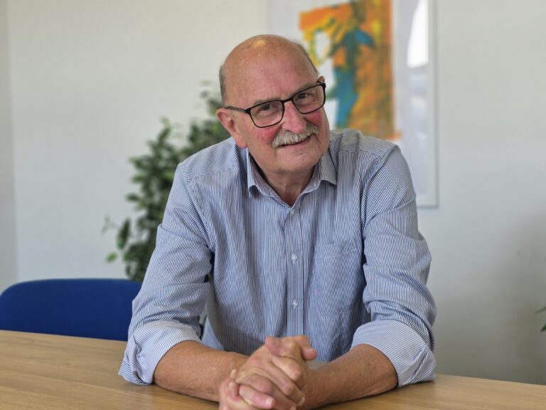 Andy Street, FareShare South West Chair of Trustees and founder. Andy is a whote man with a moustache, wearing a blue collared shirt and sitting at a desk.
