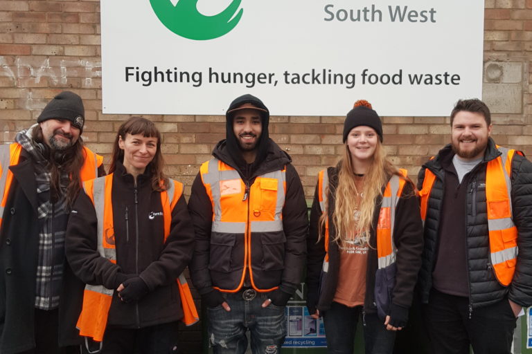 Group of employees from FareShare South West standing outside their south bristol warehouse smiling and looking at the camera.