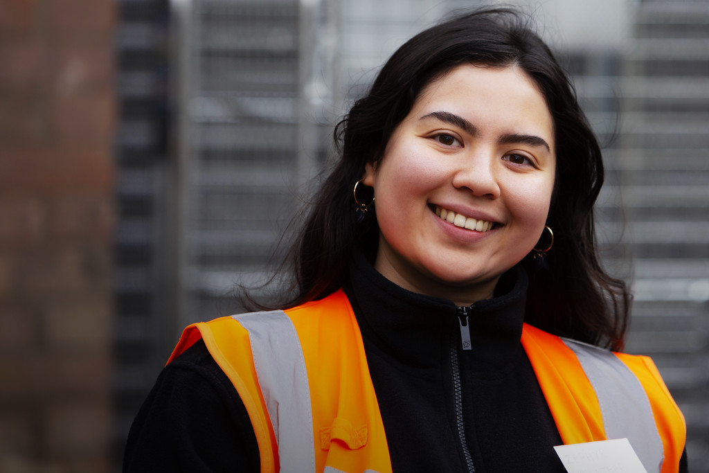 A person with long dark hair, smiling in a hi-vis jacket.