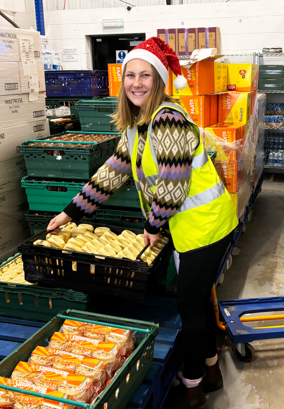 Fareshare South West getting festive: a person wearing high-vis and a santa hat moves a crate of food.