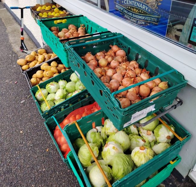 Close up on two tiers of green crates filled with fruit and vegetables. They are displayed outside a shop window
