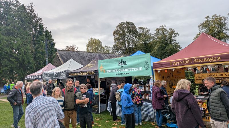 Crowds of people lining up at a row of food stalls selling sausages, charcuterie, cinnamon nuts, rum, and garlic.